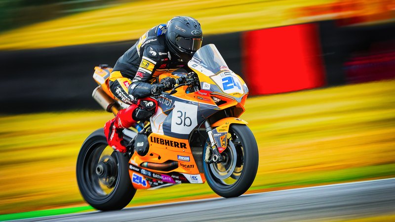 Superbike racing: Oliver Barr on the orange No. 24 Liebherr Ducati, panned against yellow and red streaks, Snetterton 2026